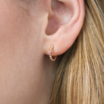 Boucle d'oreille en or rose 18 carats en forme de créole perlé ainsi qu'une barrette en or rose sertie d'un saphir rose, porté sur l'oreille d'un modèle.