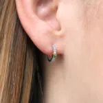 boucle d'oreille en or blanc 18 carats en forme de créole sertie de diamants ainsi qu'une barrette en or rose sertie d'un grenat vert, porté sur l'oreille d'un modèle.