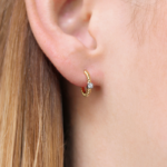 Boucle d'oreille en or jaune 18 carats en forme de créole torsadé ainsi qu'une barrette en or blanc sertie d'un diamant, porté sur l'oreille d'un modèle.