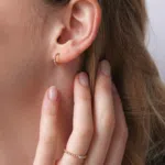 Boucle d'oreille en or rose 18 carats en forme de créole perlé ainsi qu'une barrette en or rose sertie d'un saphir rose, porté sur l'oreille d'un modèle.