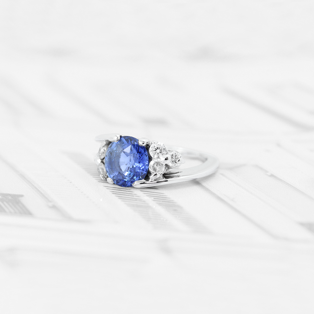 Bague en or blanc 18 carats sertie d'un saphir bleu en pierre de centre et 6 diamants autour du saphir.