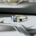 Bague vue de profil en or jaune 18 carats sertie d'un saphir bleu en pierre de centre, entouré de 4 diamants et de 2 autres saphirs bleus.