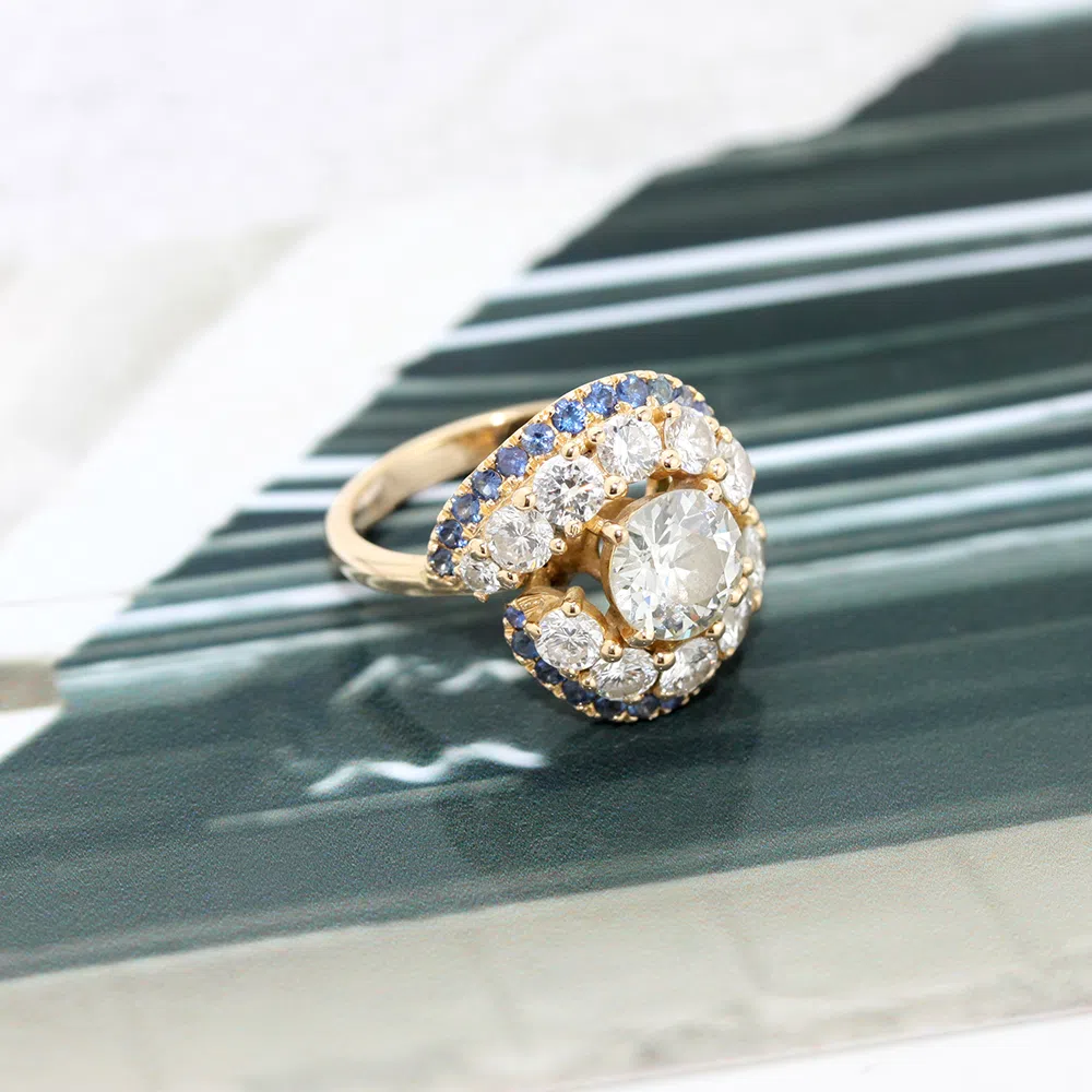 Bague en or jaune 18 carats avec un diamant en pierre de centre entouré d'une rangée de diamants, puis d'une autre rangé de saphirs bleus.