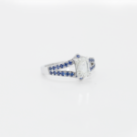 Bague en or blanc 18 carats sertie de saphirs bleus sur les anneaux en V, sublimé par un diamant en pierre de centre.