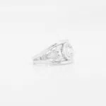 Bague en or blanc 18 carats composée de deux anneaux en forme de v comprenant un diamant au centre de ces anneaux et de deux fleurs en forme de diamants autour de ce saphir bleu.