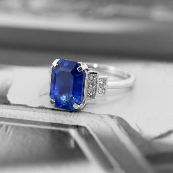 Bague art déco en or blanc 18 carats serti d'un saphir bleu en pierre de centre taillé en émeraude et de diamants autour de ce saphir.