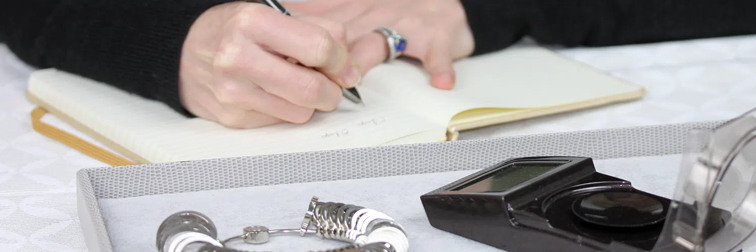Une personne en train d'écrire sur un cahier, avec devant elle des appareils de joaillerie.