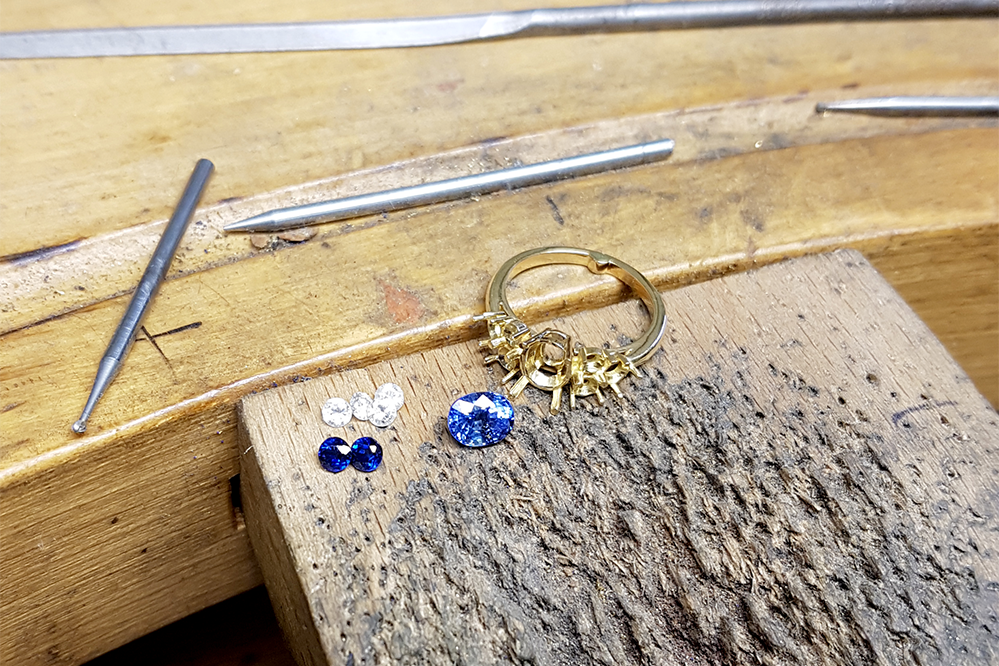 Bague en cours de fabrication en or jaune 18 carats juste avant le sertissage. Il y a des saphirs bleus et des diamants juste à côté.