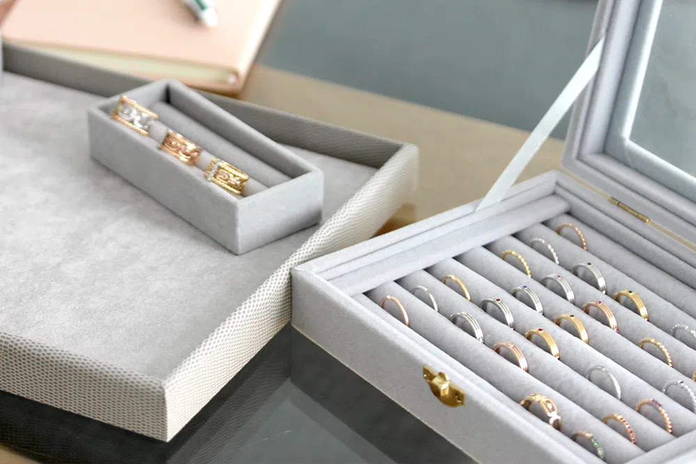 Boite à rangement pour bagues grise avec une autre boite à rangement pour bagues plus petite à côté et un tapis pour bijoux de couleur grise.