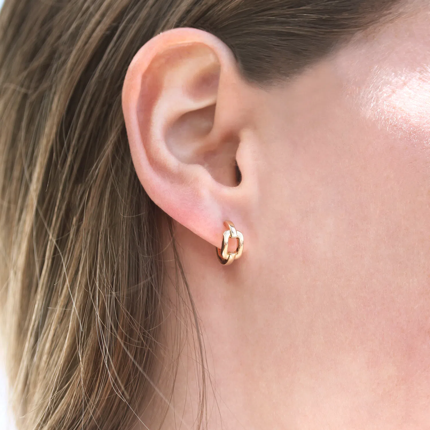 Paire de boucles d'oreilles en forme de maillon en or rose 18 carats porté aux oreilles d'une femme blonde.