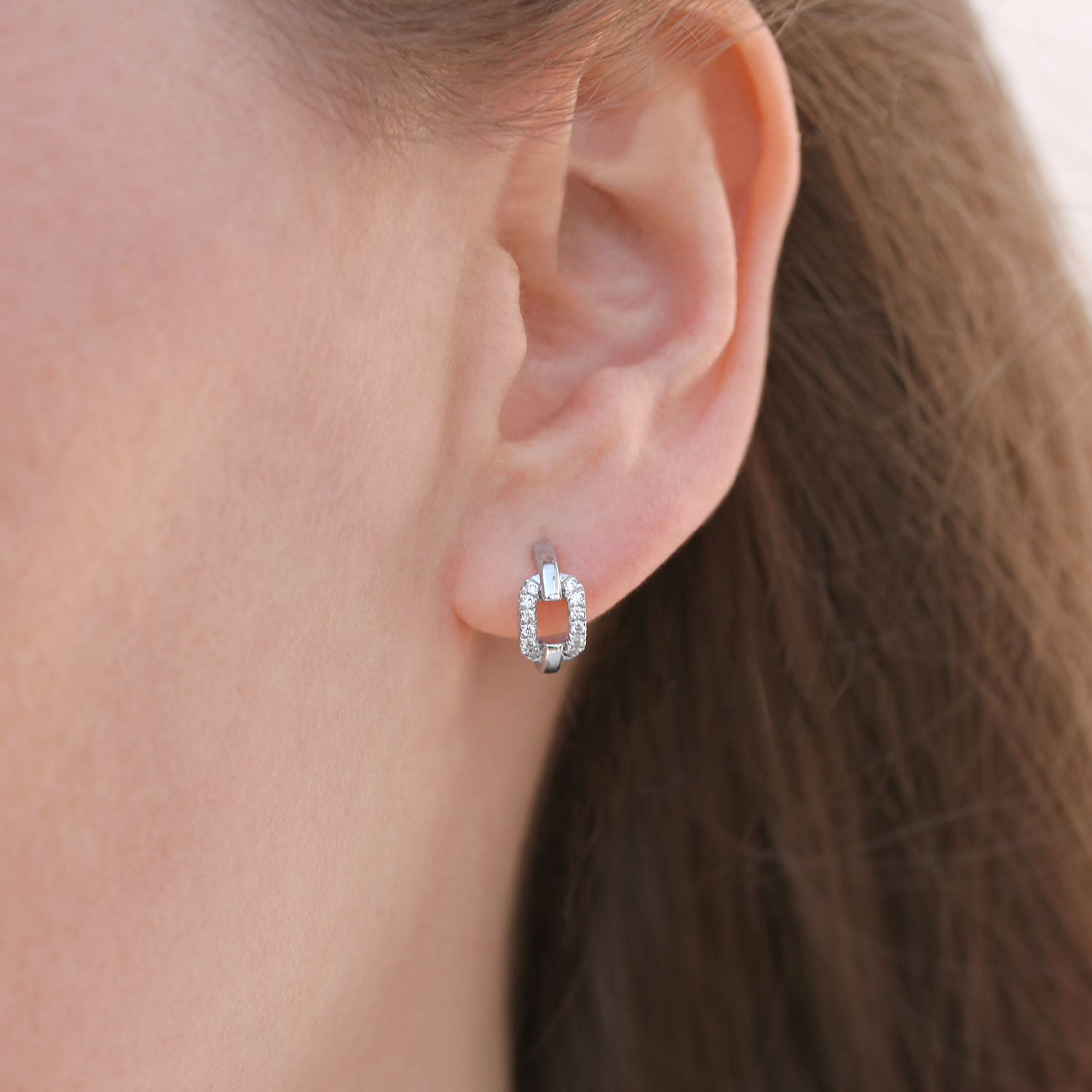 Paire de boucles d'oreilles en forme de maillon en or blanc 18 carats serti de diamants porté aux oreilles d'une femme blonde.