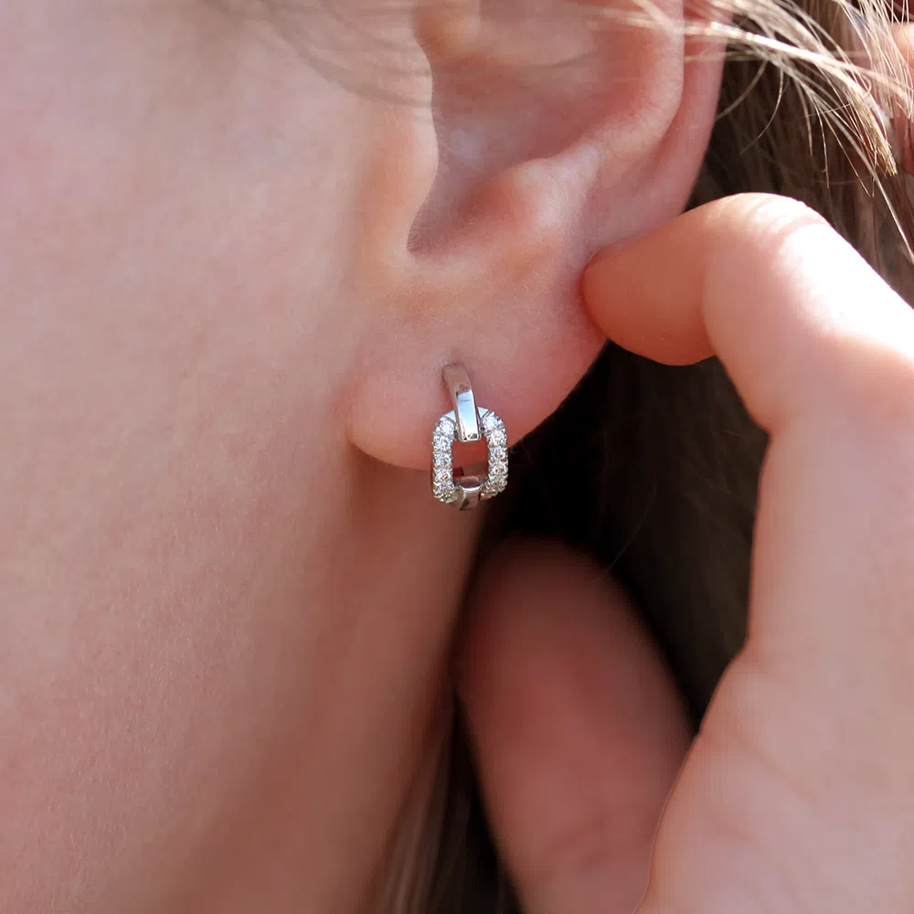 Paire de boucles d'oreilles en forme de maillon en or blanc 18 carats serti de diamants porté aux oreilles d'une femme blonde.